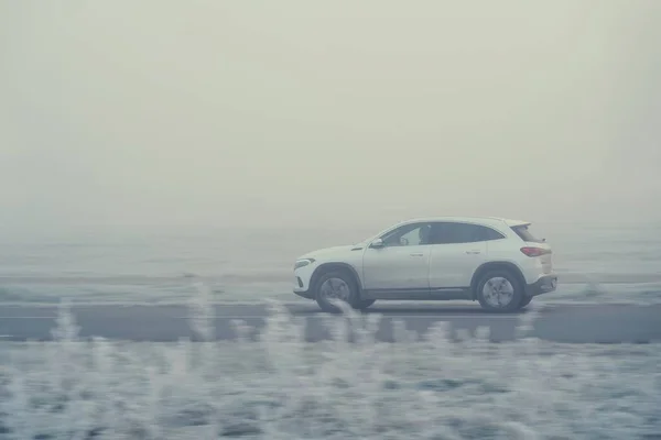 Riga, Latvia - November 15, 2021: White and dirty car drives on the foggy road, motion-blurred background, vintage look