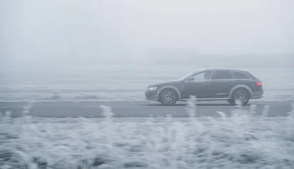 Riga, Latvia - November 15, 2021: Audi A4 Allroad Quattro driving fast on a foggy road during the cold autumn morning. Frozen grass in the foreground.  Motion blurred background.