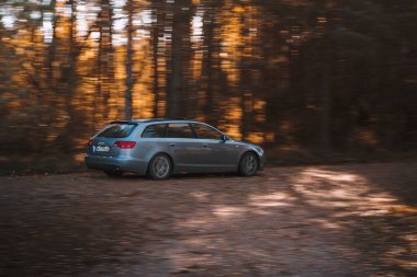 Riga, Letonya 21 Ekim 2021: Güneşli bir sonbahar gününde hızlı sürüş Audi A6 3.0 TDI Quattro, bulanık orman arka planı