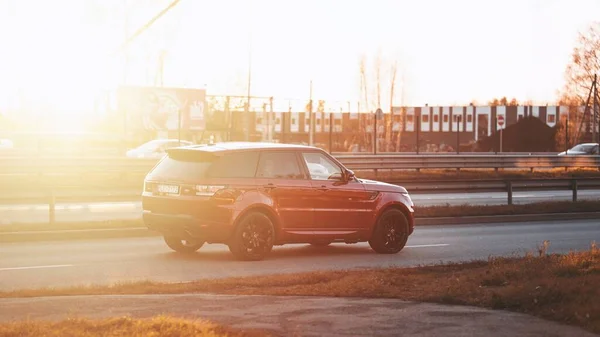 Riga, Letonya - 12 Kasım 2021: Kırmızı Range Rover Sport güneşli bir akşamda yolda araba sürüyor, altın saat