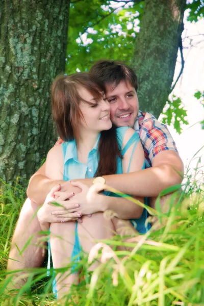 Smiling couple resting near a tree — Stock Photo, Image