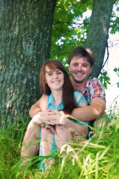 Casal sorridente descansando perto de uma árvore — Fotografia de Stock