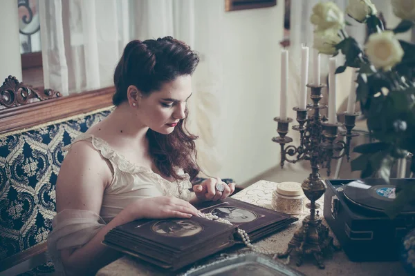 Jonge vrouw kijkt naar een fotoalbum. Vintage stijl, retro interieur. — Stockfoto
