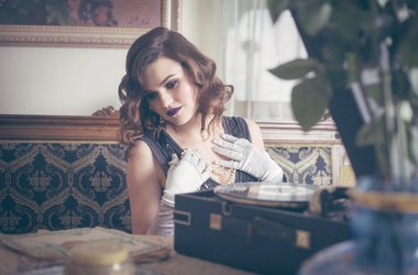 Eski tarz güzel bir kadın vinil bir pikabın yanında. Eski moda iç mekan. Stüdyo fotoğrafı.