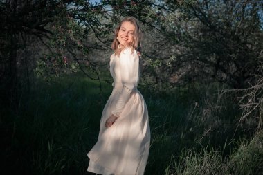 Bahçedeki güzel kadın, çiçek açan elma ağaçlarının arasında, eski moda bir elbiseyle. Bahar ya da yaz, güneşli gün.