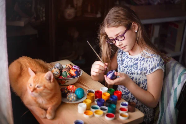 Dospívající Dívka Maluje Velikonoční Vajíčka Její Zrzavá Kočka Leží Stole — Stock fotografie
