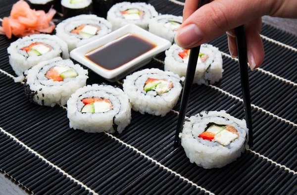 A mão da mulher a tomar sushi de Filadélfia. Tapete preto no fundo — Fotografia de Stock