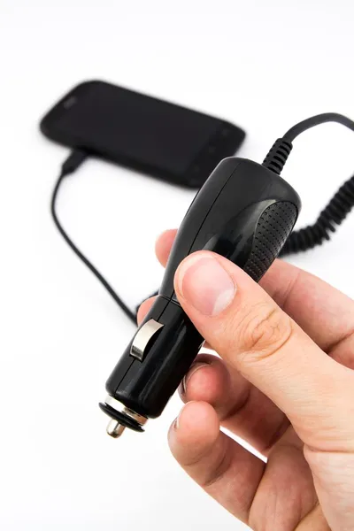 Hand holding car charger. Cell phone in background — Stock Photo, Image
