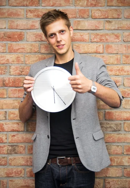 Young businessman holding a clock on brick wall background — Stock Photo, Image