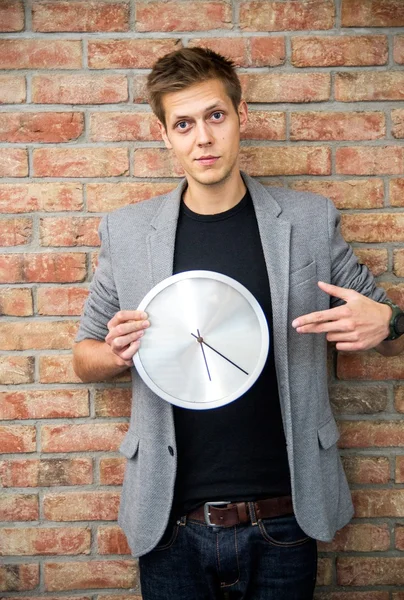 Young businessman holding a clock on brick wall background. — Stock Photo, Image