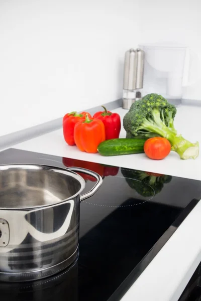 Pot and vegetables in modern kitchen with induction stove — Stock Photo, Image