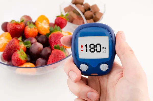 Hand met meter met waarschuwing bloedglucose niveau test. fruit in ba — Stockfoto