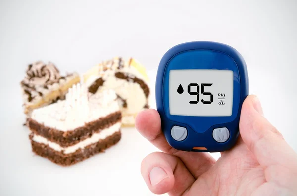 Hand holding meter. Diabetes doing glucose level test. Cake in b — Stock Photo, Image