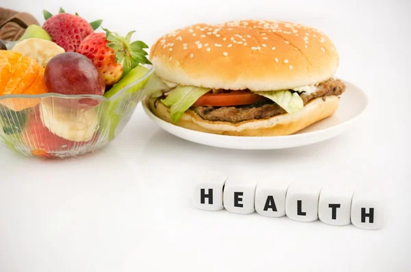 Gezondheid woord over dobbelstenen. Hamburger en fruit in babkground — Stockfoto