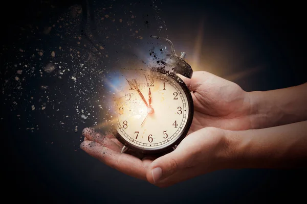 Concept of passing away, the clock breaks down into pieces. Hand holding analog clock with dispersion effect