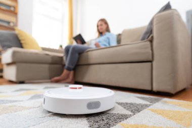 Modern robot elektrikli süpürge. Otonom robot daireyi temizliyor, genç kadının boş vakti var.