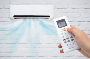 Air conditioning and a stream of fresh cold air. Hand holding remote control.