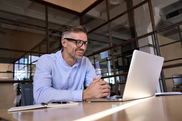 Happy mature business man looking at laptop having virtual meeting in office.