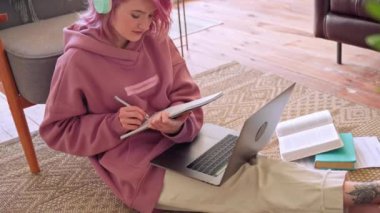 Pembe saçlı üniversiteli genç kız laptopta öğreniyor. Evde yerde oturuyor..