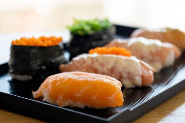 Dikilmiş maki ve somon nigiri suşisi beyaz arka planda siyah geleneksel tepsiye yakın.
