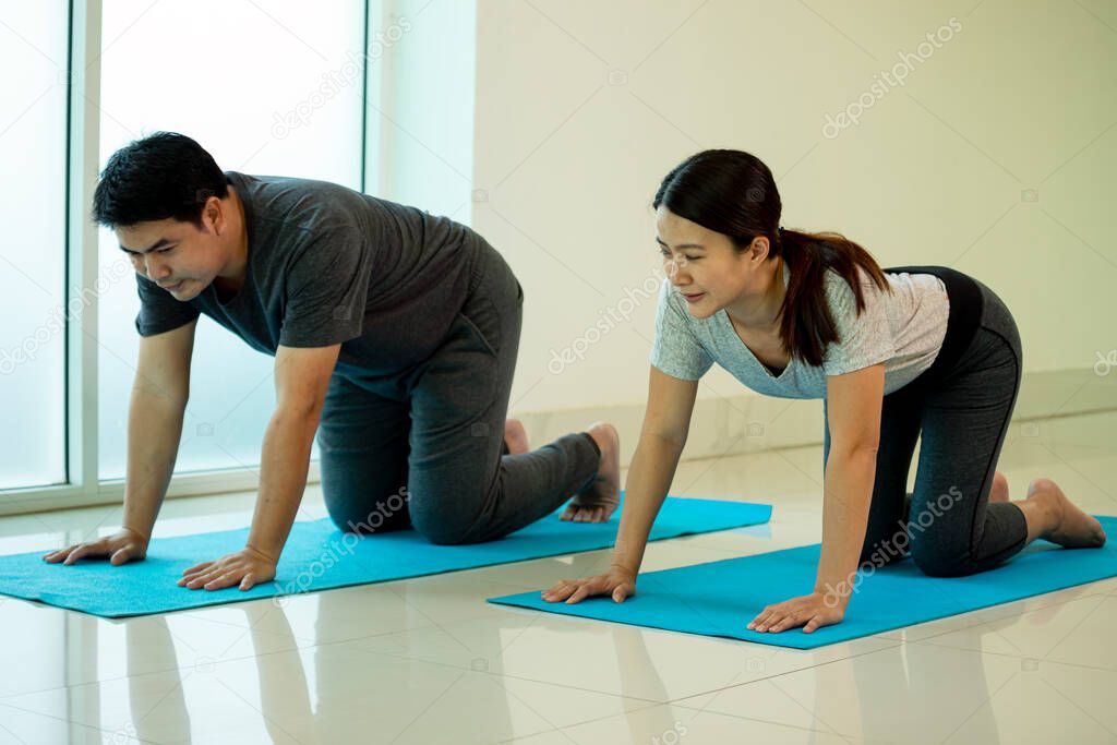 Two Asian young couple adult practice Yoga pose Box or Chakravakasana on blue mat in gym near window following training vdo from laptop