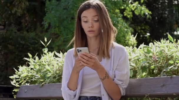 Bankta Oturan Üzgün Genç Bir Kadın Telefondaki Kötü Haberleri Okuyor — Stok video