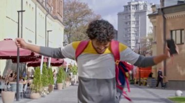 Mutlu ve pozitif genç adam sokakta ayakta ve dans ediyor. Müzik dinlemek ve eğlenmek. Yavaş çekim.