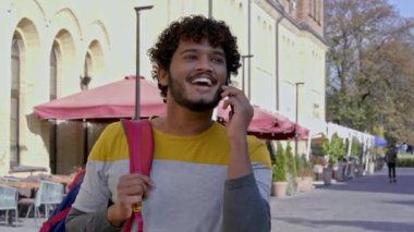 Gülümseyen genç adam sokakta yürüyor, telefonla konuşuyor ve arıyor. Yavaş çekim.