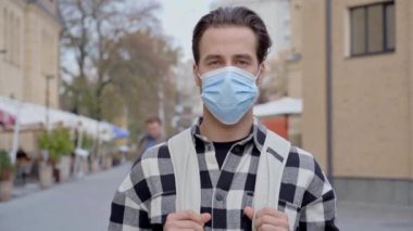 Sırt çantalı ve koruyucu maskeli bir adam caddede kameraya bakıyor. Yavaş çekim.