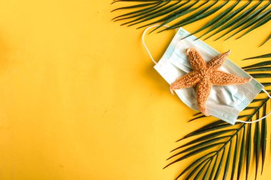 Deniz yıldızı ve sarı arka planda tıbbi maske. Metin için alanı kopyala. Coronavirus seyahat kavramı