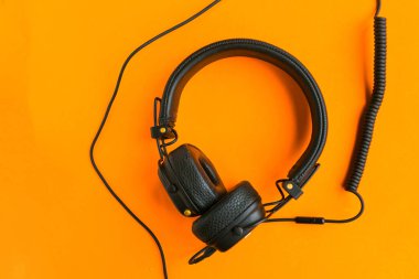 Turuncu arka planda büyük profesyonel kulaklıklar. Müzik dinlemek, sosyal ağlar rahatlamaya yol açar..