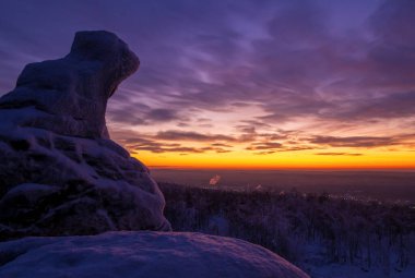 Karlı çam ağaçlarıyla kaplı Ural dağlarının kayaları ve taşları üzerinde destansı kırmızı günbatımı