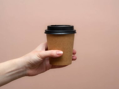Kadın elleri pembe arka planda kağıt bardak tutuyor. Boşluğu kopyala.