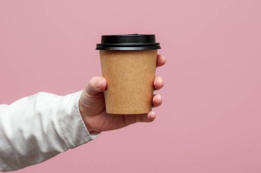 Kadın elleri pembe arka planda kağıt bardak tutuyor. Boşluğu kopyala.