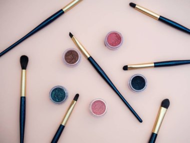Dekoratif makyaj ürünleri içeren kompozisyon altın fırçalar ve pastel pembe arka planda renkli göz gölgeleri.
