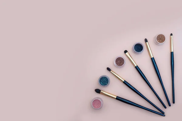 Composición con productos de maquillaje decorativos cepillos dorados y sombras coloridas de ojos sobre fondo rosa pastel. — Foto de Stock
