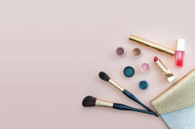 Pembe arka planda altın makyaj çantasından görünen kozmetik ürünleri. Fotoğraf.