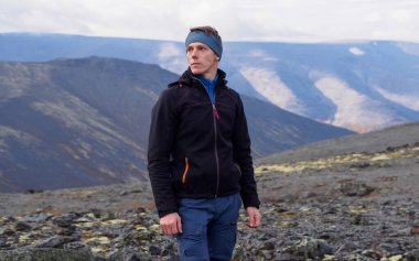 Bir bandana içinde yürüyüş direkleri olan genç bir adam, dağların arka planına karşı duruyor. fotoğraf