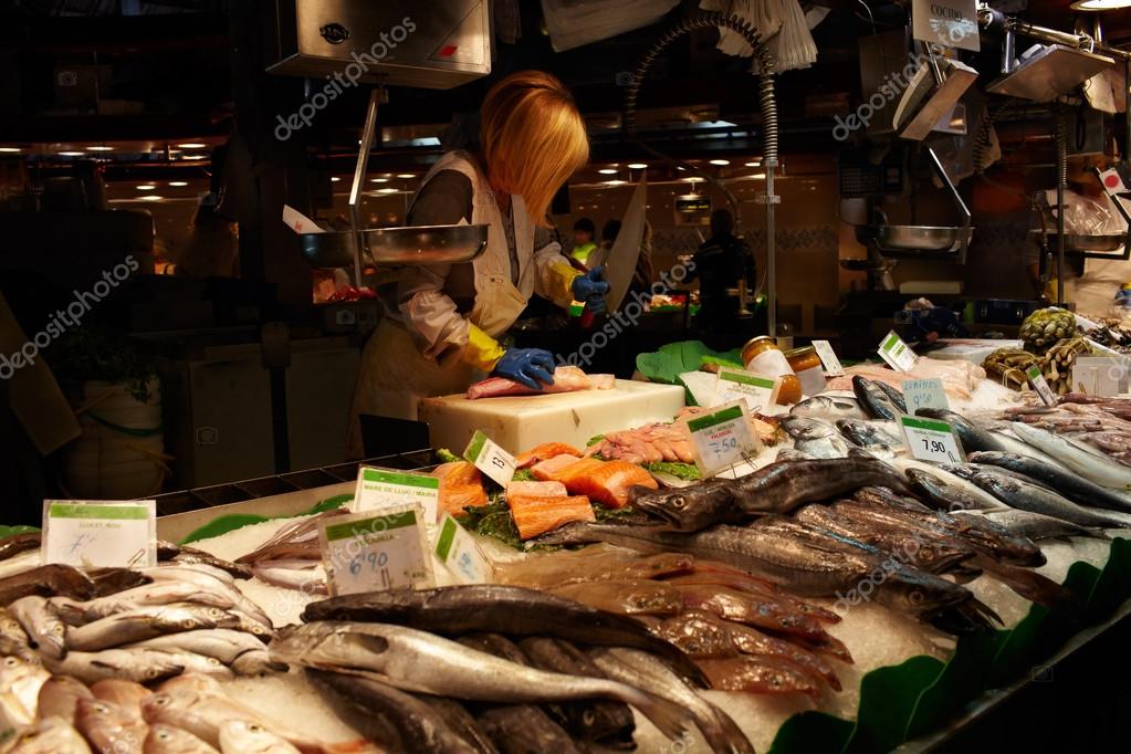The fish seller in a fish section of the market is cutting a fish with a knife. No visible faces, logos or TM's