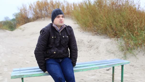 Un joven está sentado en el banco y mirando al mar . — Vídeos de Stock