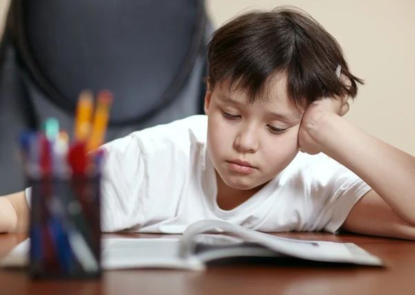 School jongen studies hard over zijn boek thuis. — Stockfoto