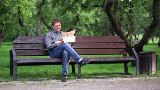 Man leest de krant op bankje in het park — Stockvideo