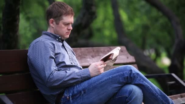 Άνθρωπος διαβάζει εφημερίδα σε παγκάκι στο πάρκο — Αρχείο Βίντεο