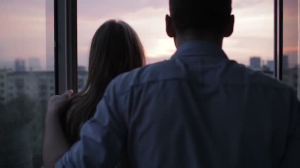 Mann und Frau stehen am Fenster und beobachten den Sonnenuntergang — Stockvideo