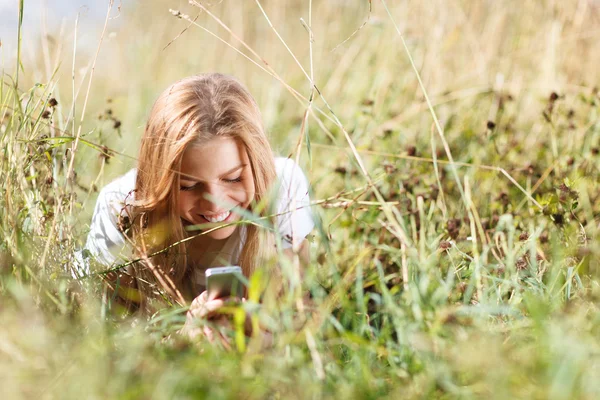 Meisje is het schrijven van sms op de telefoon liggen in gras — Stockfoto