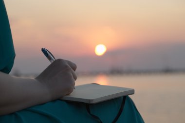 Woman writing in her diary at sunset clipart