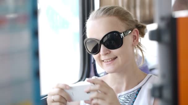 Giovane donna che indossa occhiali da sole reggendo e fotografando al suo cellulare — Video Stock