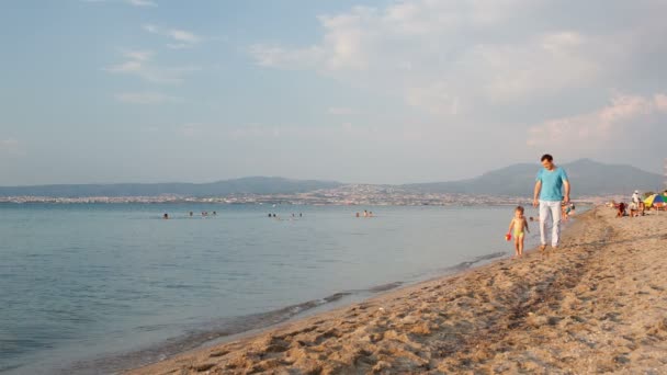 Padre y su pequeño hijo caminando por la playa al borde del agua — Vídeos de Stock