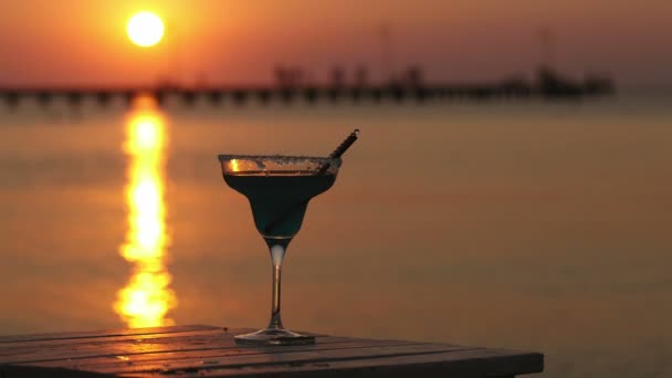 Lass van tropische cocktail staande op een houten tafel met uitzicht op een zonsondergang — Stockvideo