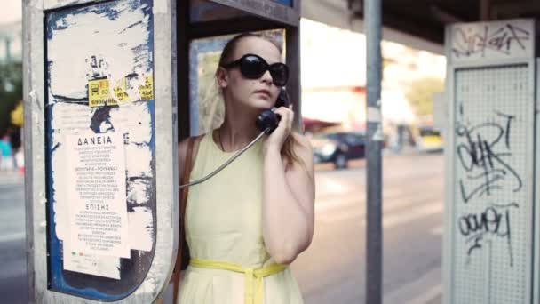 Attraktive Frau mit Sonnenbrille plaudert an einem öffentlichen Telefon in einer städtischen Straße — Stockvideo